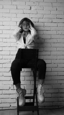 Beyaz tişörtlü, siyah beyaz saçlı, güzel ve seksi bir kadının stüdyoda beyaz bir duvara poz verdiği siyah beyaz bir fotoğraf..  