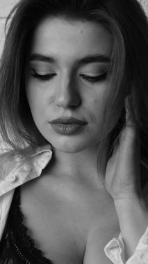 Beyaz tişörtlü, siyah beyaz saçlı, güzel ve seksi bir kadının stüdyoda beyaz bir duvara poz verdiği siyah beyaz bir fotoğraf..  