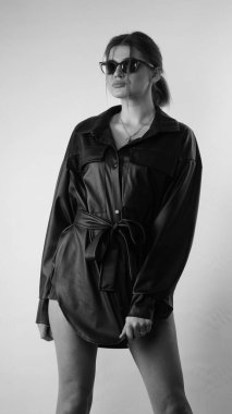 Siyah gömlekli ve güneş gözlüklü genç bir kadının stüdyoda poz verirken çekilmiş siyah beyaz bir fotoğrafı..  