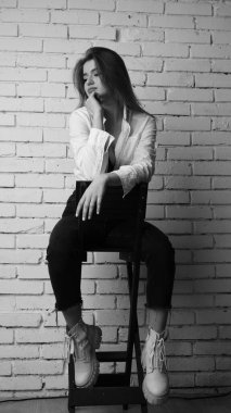 Beyaz tişörtlü, siyah beyaz saçlı, güzel ve seksi bir kadının stüdyoda beyaz bir duvara poz verdiği siyah beyaz bir fotoğraf..  