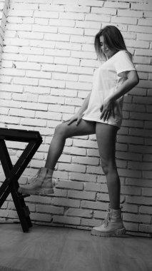 Stüdyoda sandalyenin yanında uzun saçlı, siyah beyaz bir kadın poz veriyor..  