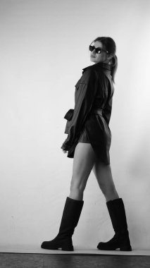 Siyah gömlekli ve güneş gözlüklü genç bir kadının stüdyoda poz verirken çekilmiş siyah beyaz bir fotoğrafı..  