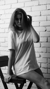 Stüdyoda sandalyenin yanında uzun saçlı, siyah beyaz bir kadın poz veriyor..  