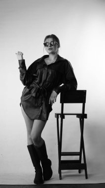 Siyah gömlekli ve güneş gözlüklü genç bir kadının stüdyoda poz verirken çekilmiş siyah beyaz bir fotoğrafı..  