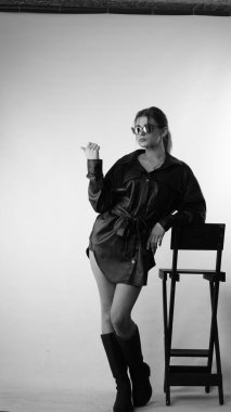 Siyah gömlekli ve güneş gözlüklü genç bir kadının stüdyoda poz verirken çekilmiş siyah beyaz bir fotoğrafı..  