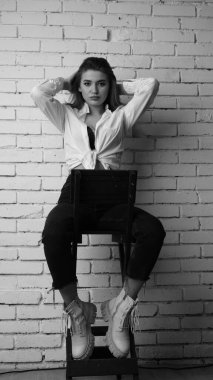 Beyaz tişörtlü, siyah beyaz saçlı, güzel ve seksi bir kadının stüdyoda beyaz bir duvara poz verdiği siyah beyaz bir fotoğraf..  