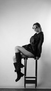 Siyah gömlekli ve güneş gözlüklü genç bir kadının stüdyoda poz verirken çekilmiş siyah beyaz bir fotoğrafı..  