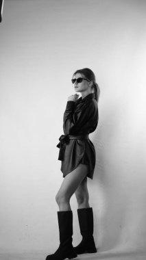 Siyah gömlekli ve güneş gözlüklü genç bir kadının stüdyoda poz verirken çekilmiş siyah beyaz bir fotoğrafı..  