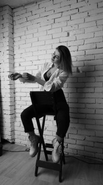 Beyaz tişörtlü, siyah beyaz saçlı, güzel ve seksi bir kadının stüdyoda beyaz bir duvara poz verdiği siyah beyaz bir fotoğraf..  