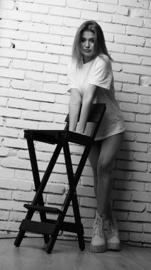 Stüdyoda sandalyenin yanında uzun saçlı, siyah beyaz bir kadın poz veriyor..  