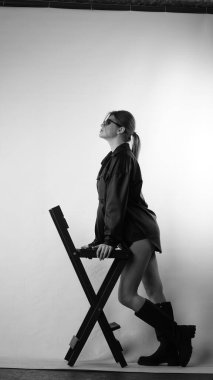 Siyah gömlekli ve güneş gözlüklü genç bir kadının stüdyoda poz verirken çekilmiş siyah beyaz bir fotoğrafı..  