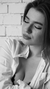 Beyaz tişörtlü, siyah beyaz saçlı, güzel ve seksi bir kadının stüdyoda beyaz bir duvara poz verdiği siyah beyaz bir fotoğraf..  