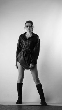 Siyah gömlekli ve güneş gözlüklü genç bir kadının stüdyoda poz verirken çekilmiş siyah beyaz bir fotoğrafı..  