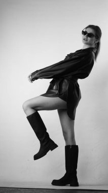 Siyah gömlekli ve güneş gözlüklü genç bir kadının stüdyoda poz verirken çekilmiş siyah beyaz bir fotoğrafı..  