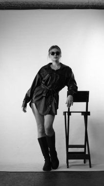 Siyah gömlekli ve güneş gözlüklü genç bir kadının stüdyoda poz verirken çekilmiş siyah beyaz bir fotoğrafı..  