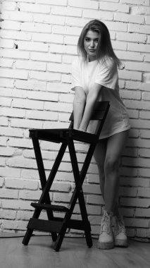 Stüdyoda sandalyenin yanında uzun saçlı, siyah beyaz bir kadın poz veriyor..  