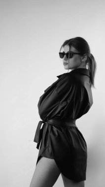 Stüdyoda siyah gömlek ve güneş gözlüğü takan güzel bir kadının siyah beyaz fotoğrafı..  