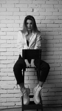 Beyaz tişörtlü, siyah beyaz saçlı, güzel ve seksi bir kadının stüdyoda beyaz bir duvara poz verdiği siyah beyaz bir fotoğraf..  