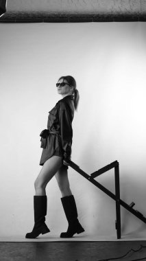 Siyah gömlekli ve güneş gözlüklü genç bir kadının stüdyoda poz verirken çekilmiş siyah beyaz bir fotoğrafı..  