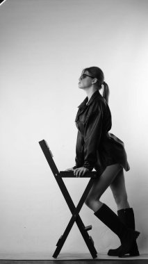 Siyah gömlekli ve güneş gözlüklü genç bir kadının stüdyoda poz verirken çekilmiş siyah beyaz bir fotoğrafı..  