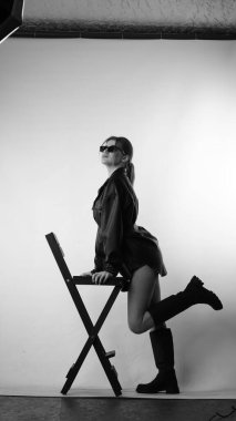 Siyah gömlekli ve güneş gözlüklü genç bir kadının stüdyoda poz verirken çekilmiş siyah beyaz bir fotoğrafı..  