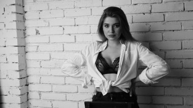 Beyaz tişörtlü, siyah beyaz saçlı, güzel ve seksi bir kadının stüdyoda beyaz bir duvara poz verdiği siyah beyaz bir fotoğraf..  