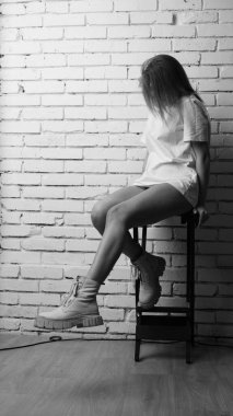 Stüdyoda sandalyenin yanında uzun saçlı, siyah beyaz bir kadın poz veriyor..  