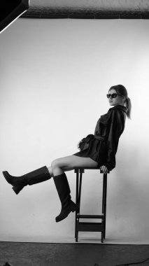 Siyah gömlekli ve güneş gözlüklü genç bir kadının stüdyoda poz verirken çekilmiş siyah beyaz bir fotoğrafı..  