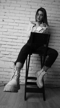 Beyaz tişörtlü, siyah beyaz saçlı, güzel ve seksi bir kadının stüdyoda beyaz bir duvara poz verdiği siyah beyaz bir fotoğraf..  