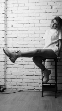 Stüdyoda sandalyenin yanında uzun saçlı, siyah beyaz bir kadın poz veriyor..  