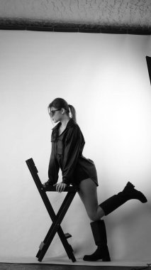 Siyah gömlekli ve güneş gözlüklü genç bir kadının stüdyoda poz verirken çekilmiş siyah beyaz bir fotoğrafı..  