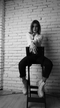 Beyaz tişörtlü, siyah beyaz saçlı, güzel ve seksi bir kadının stüdyoda beyaz bir duvara poz verdiği siyah beyaz bir fotoğraf..  