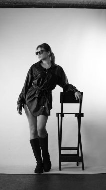 Siyah gömlekli ve güneş gözlüklü genç bir kadının stüdyoda poz verirken çekilmiş siyah beyaz bir fotoğrafı..  