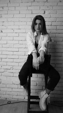 Beyaz tişörtlü, siyah beyaz saçlı, güzel ve seksi bir kadının stüdyoda beyaz bir duvara poz verdiği siyah beyaz bir fotoğraf..  