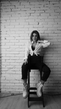 Beyaz tişörtlü, siyah beyaz saçlı, güzel ve seksi bir kadının stüdyoda beyaz bir duvara poz verdiği siyah beyaz bir fotoğraf..  