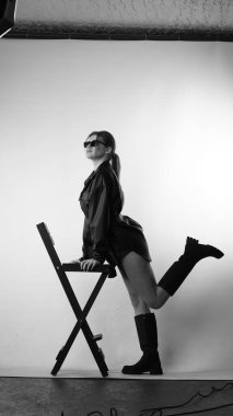 Siyah gömlekli ve güneş gözlüklü genç bir kadının stüdyoda poz verirken çekilmiş siyah beyaz bir fotoğrafı..  