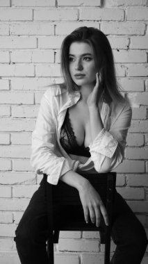 Beyaz tişörtlü, siyah beyaz saçlı, güzel ve seksi bir kadının stüdyoda beyaz bir duvara poz verdiği siyah beyaz bir fotoğraf..  