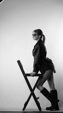 Siyah gömlekli ve güneş gözlüklü genç bir kadının stüdyoda poz verirken çekilmiş siyah beyaz bir fotoğrafı..  