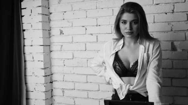 在演播室里 年轻美丽的性感性感女人身穿白衬衫 靠着一面白砖墙摆姿势的黑白照片 — 图库照片