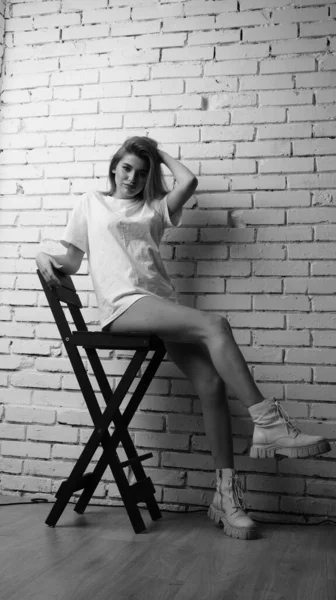 Stüdyoda sandalyenin yanında uzun saçlı, siyah beyaz bir kadın poz veriyor..  