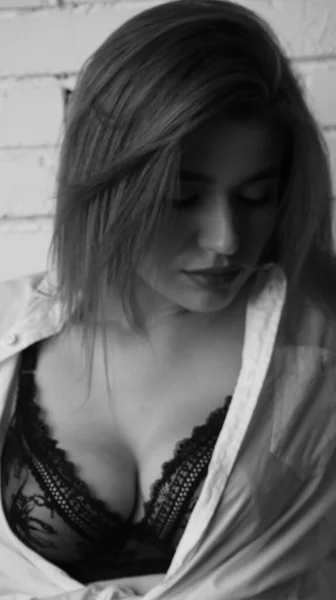 在演播室里 年轻美丽的性感性感女人身穿白衬衫 靠着一面白砖墙摆姿势的黑白照片 — 图库照片
