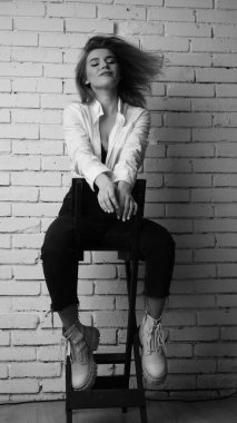 Beyaz tişörtlü, siyah beyaz saçlı, güzel ve seksi bir kadının stüdyoda beyaz bir duvara poz verdiği siyah beyaz bir fotoğraf..  