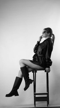 Siyah gömlekli ve güneş gözlüklü genç bir kadının stüdyoda poz verirken çekilmiş siyah beyaz bir fotoğrafı..  