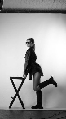 Siyah gömlekli ve güneş gözlüklü genç bir kadının stüdyoda poz verirken çekilmiş siyah beyaz bir fotoğrafı..  