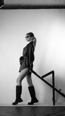 Siyah gömlekli ve güneş gözlüklü genç bir kadının stüdyoda poz verirken çekilmiş siyah beyaz bir fotoğrafı..  