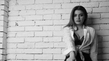 Beyaz tişörtlü, siyah beyaz saçlı, güzel ve seksi bir kadının stüdyoda beyaz bir duvara poz verdiği siyah beyaz bir fotoğraf..  