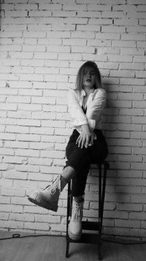 Beyaz tişörtlü, siyah beyaz saçlı, güzel ve seksi bir kadının stüdyoda beyaz bir duvara poz verdiği siyah beyaz bir fotoğraf..  