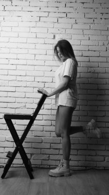 Stüdyoda sandalyenin yanında uzun saçlı, siyah beyaz bir kadın poz veriyor..  