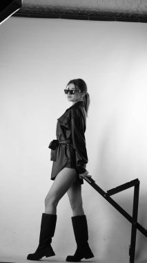 Siyah gömlekli ve güneş gözlüklü genç bir kadının stüdyoda poz verirken çekilmiş siyah beyaz bir fotoğrafı..  