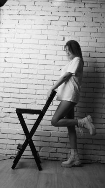 Stüdyoda sandalyenin yanında uzun saçlı, siyah beyaz bir kadın poz veriyor..  